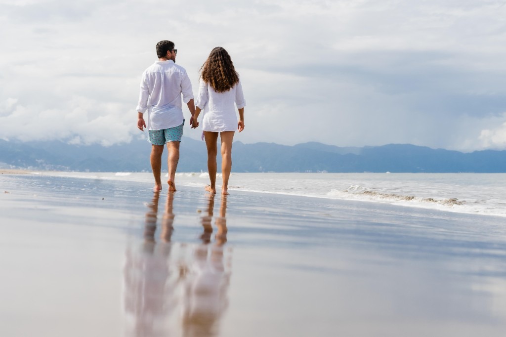 Couple walking along a sandy beach at sunset with a warm golden sky.