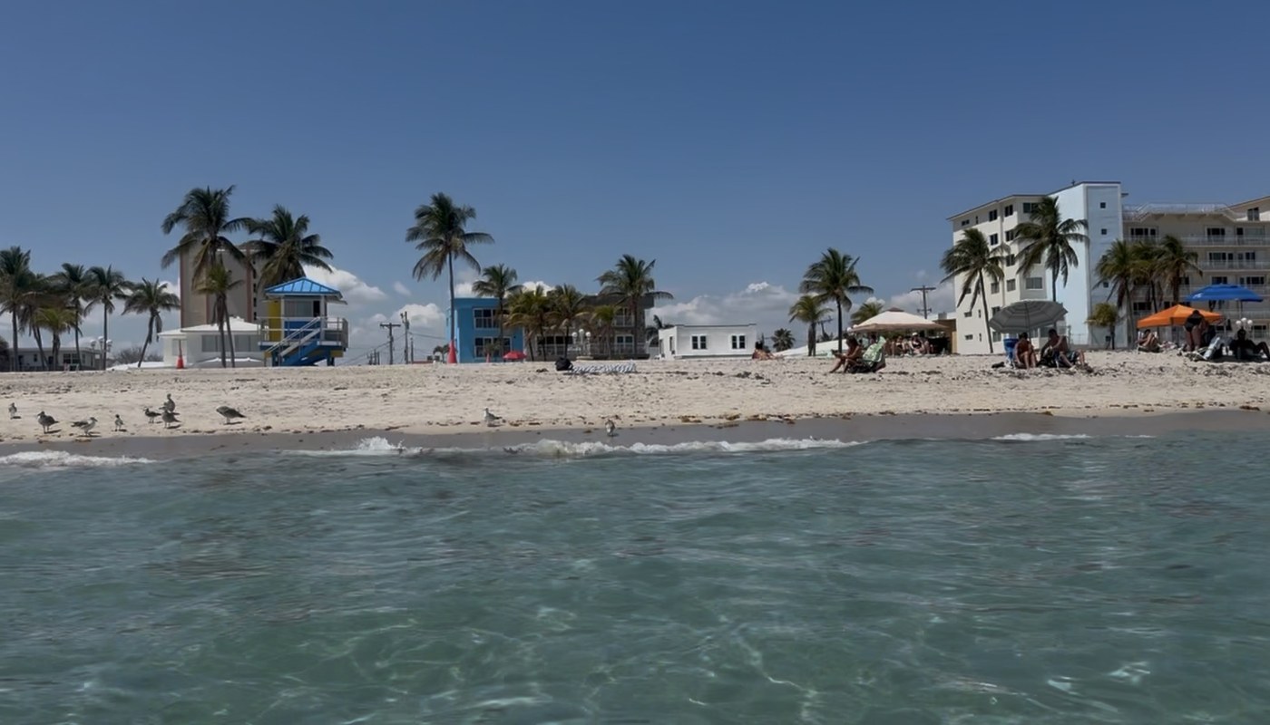 Hollywood Beach from the shallow Atlantic, turquoise water and white sand with the Broadwalk shoreline and a blue lifeguard tower