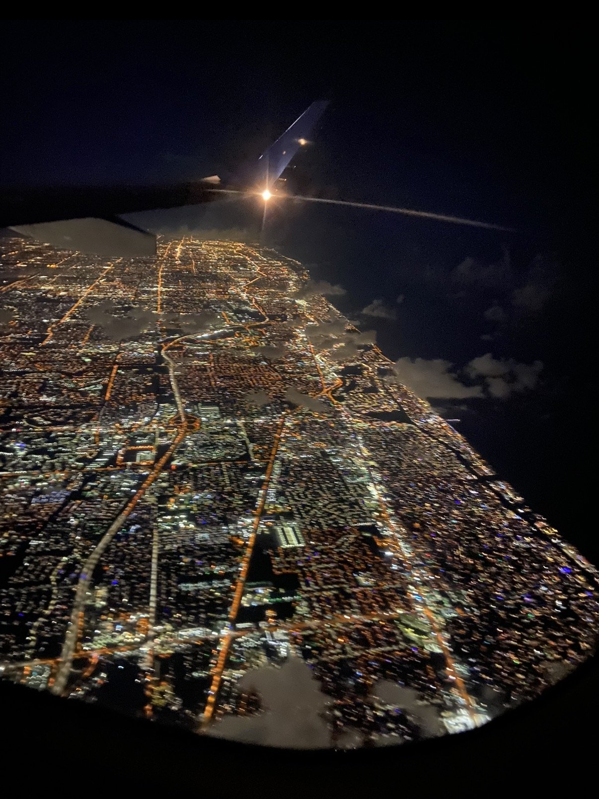 Aerial view of Miami at night from an airplane window, city lights stretching to the coast
